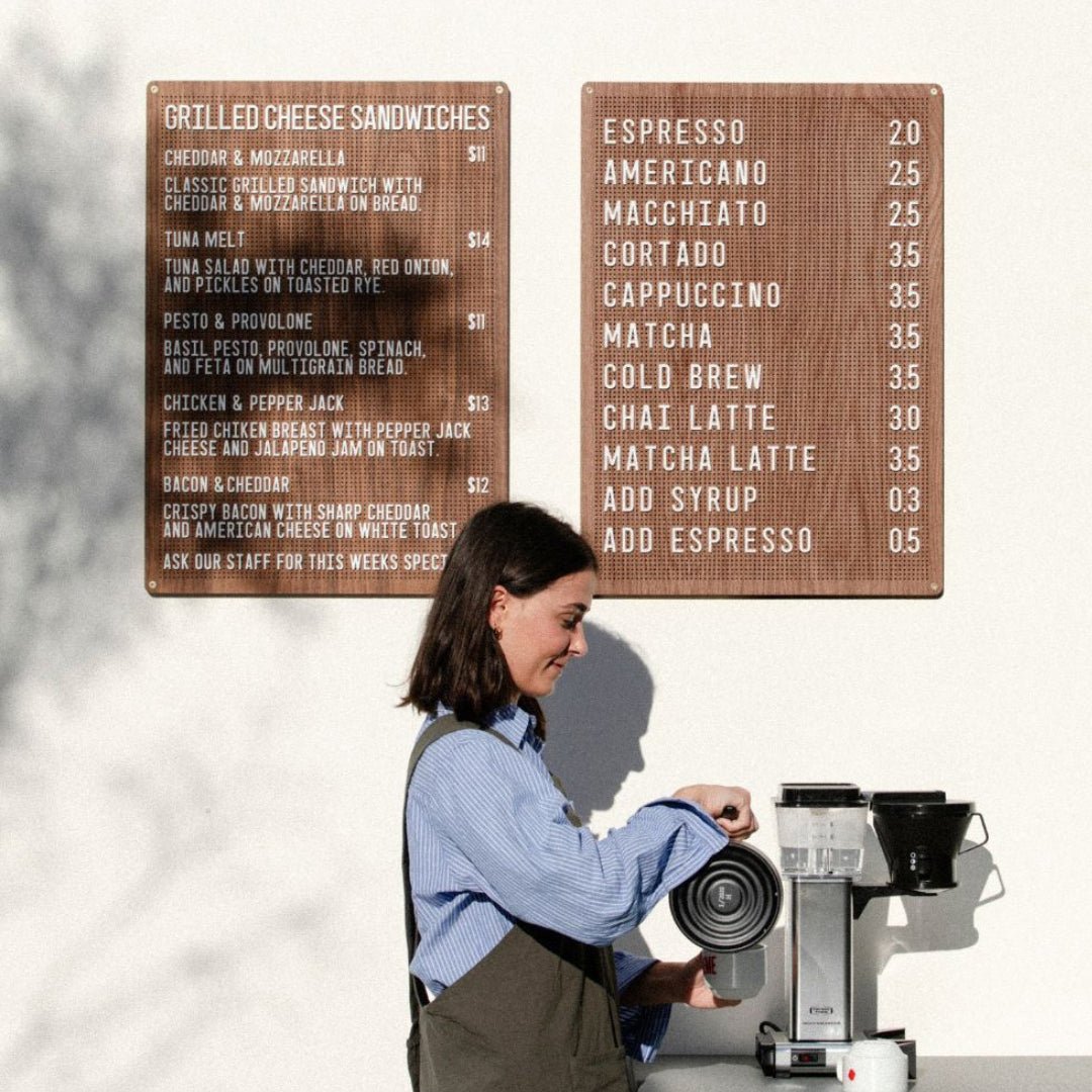 Dual wooden peg letter boards in walnut veneer with white peg letters, with woman standing in front making coffee