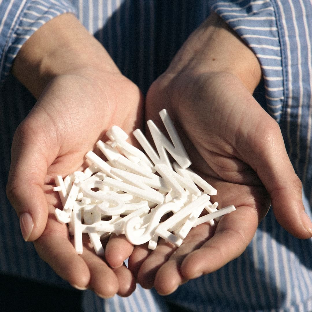 Close-up of hands holding bundle of white plastic peg letters for wooden letter board