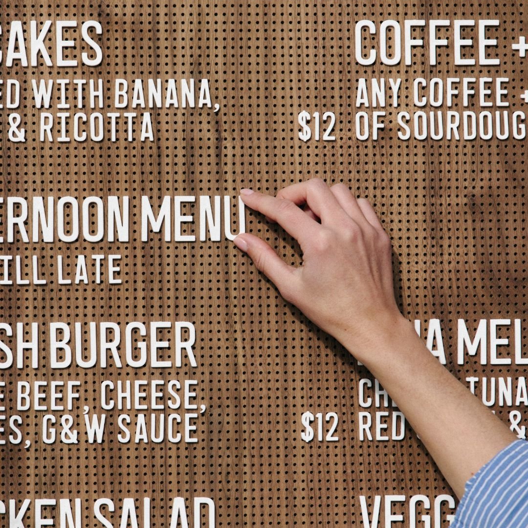Wooden peg letter board in walnut finish displaying full café menu with woman writing items in white peg letters