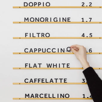 Atelier Letter Board in brass finished rails with café menu, with a hand adjusting black letters spelling cappuccino