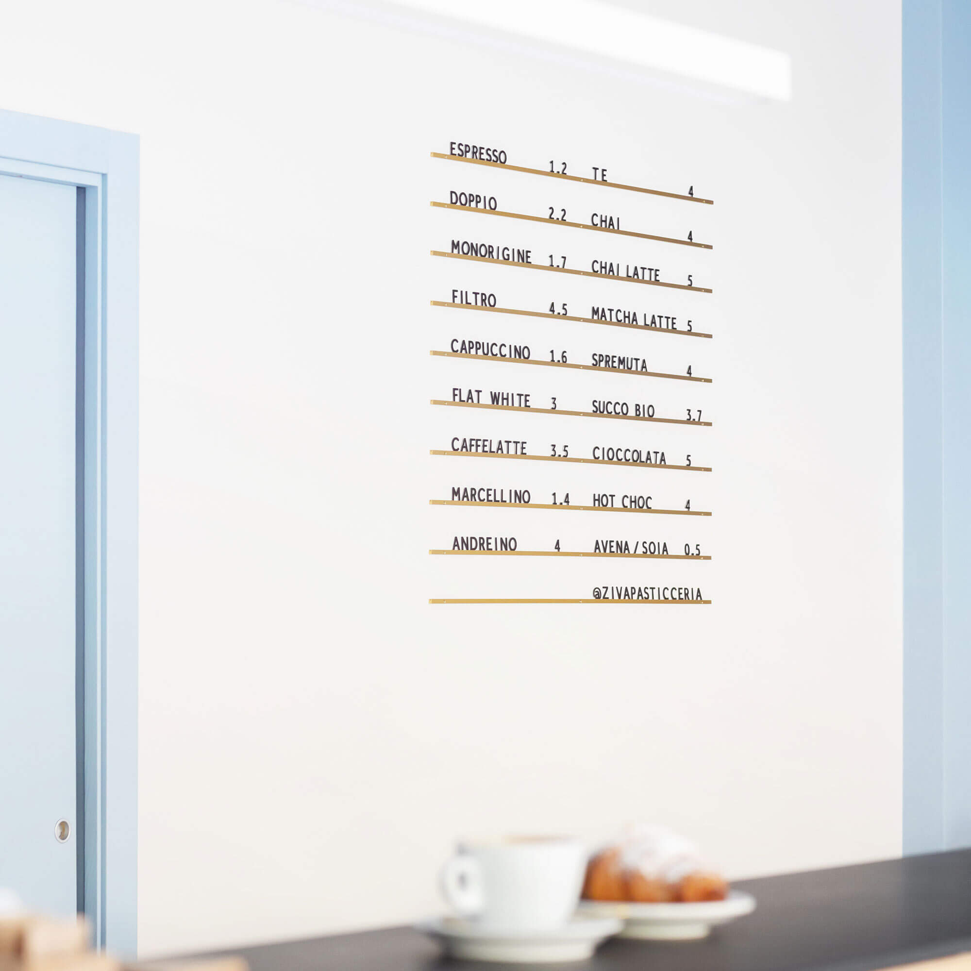 Minimal Atelier Letter Board in bronze with clean black letters, mounted on white wall with coffee on countertop