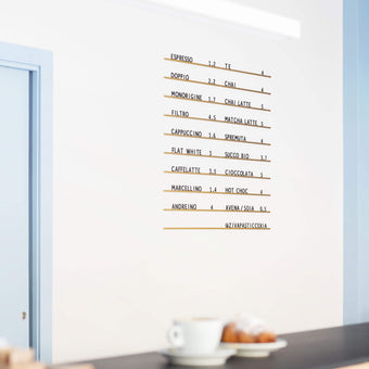 Minimal Atelier Letter Board in bronze with clean black letters, mounted on white wall with coffee on countertop