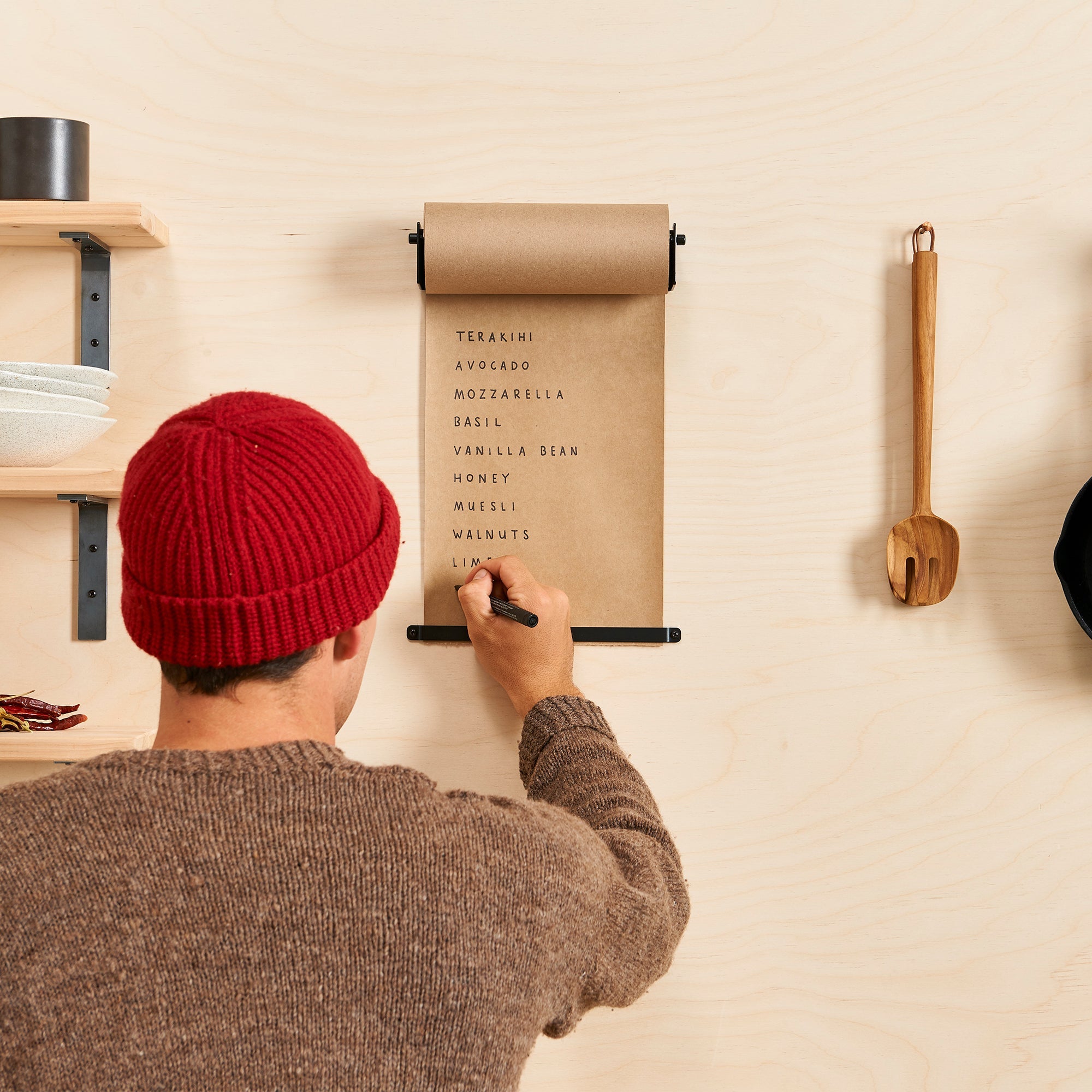 person in a red beanie writing lists on the brown kraft paper roll dispenser