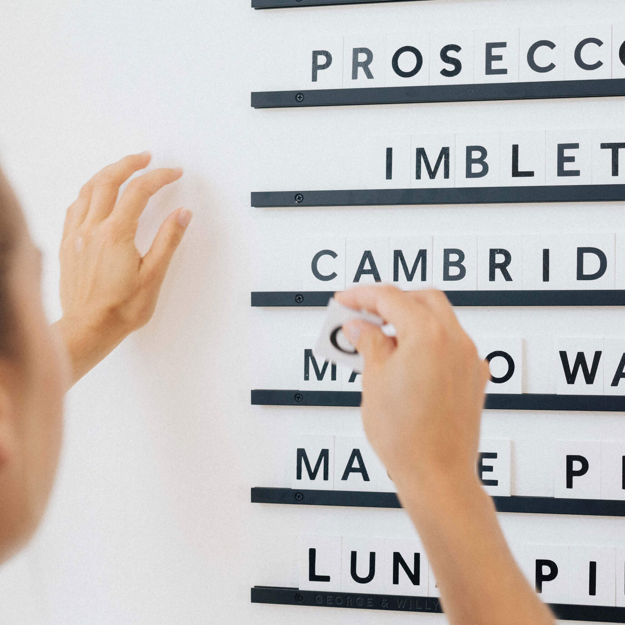 close up of small wooden letter menu board in black rails white letter tiles colourway with hand adjusting letters