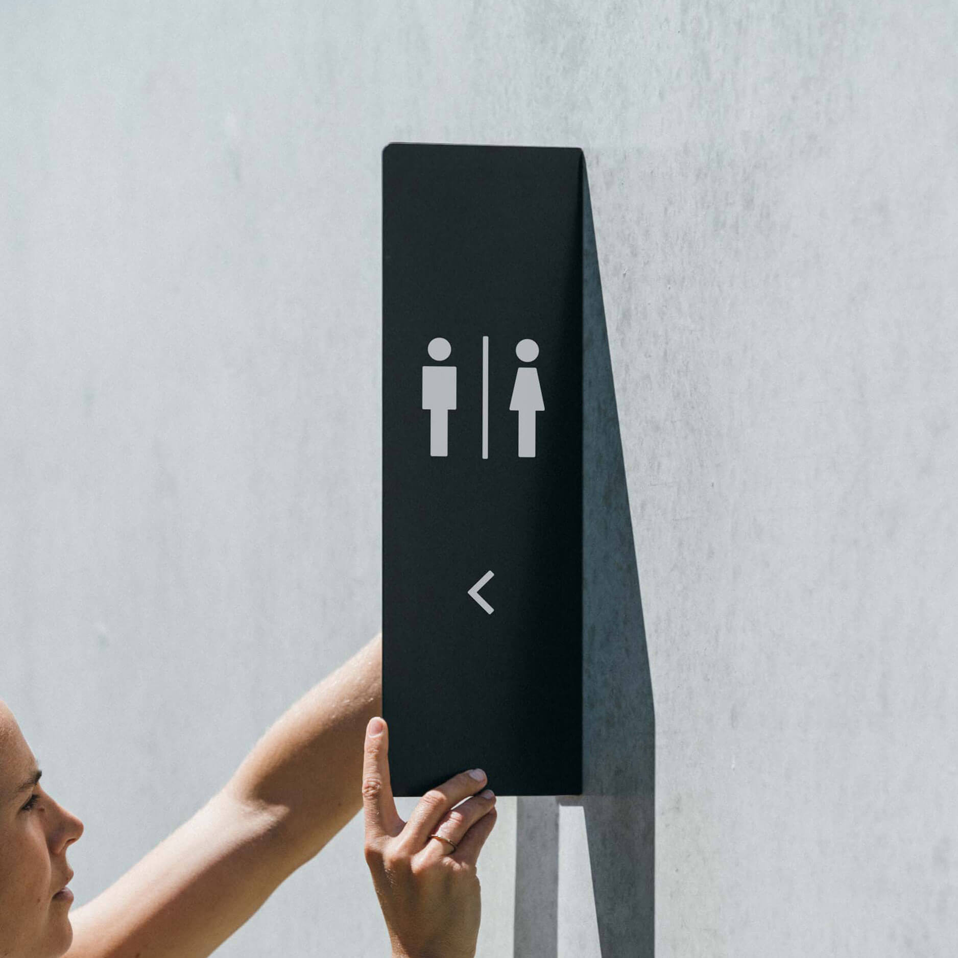 two hands holding up a vertical metal blade sign that has toilet decals on it as a bathroom sign