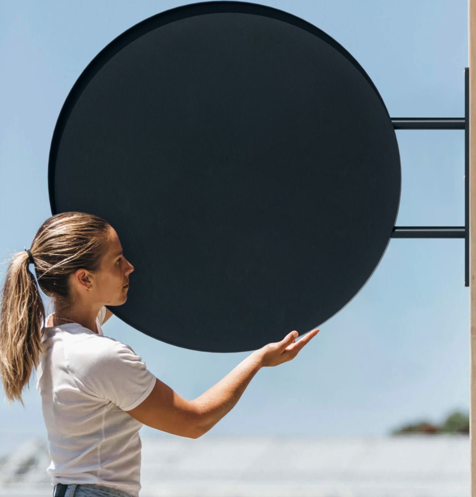 Person holding large round sign in black finish, showing scale and dimensions, preparing for wall signageinstallation