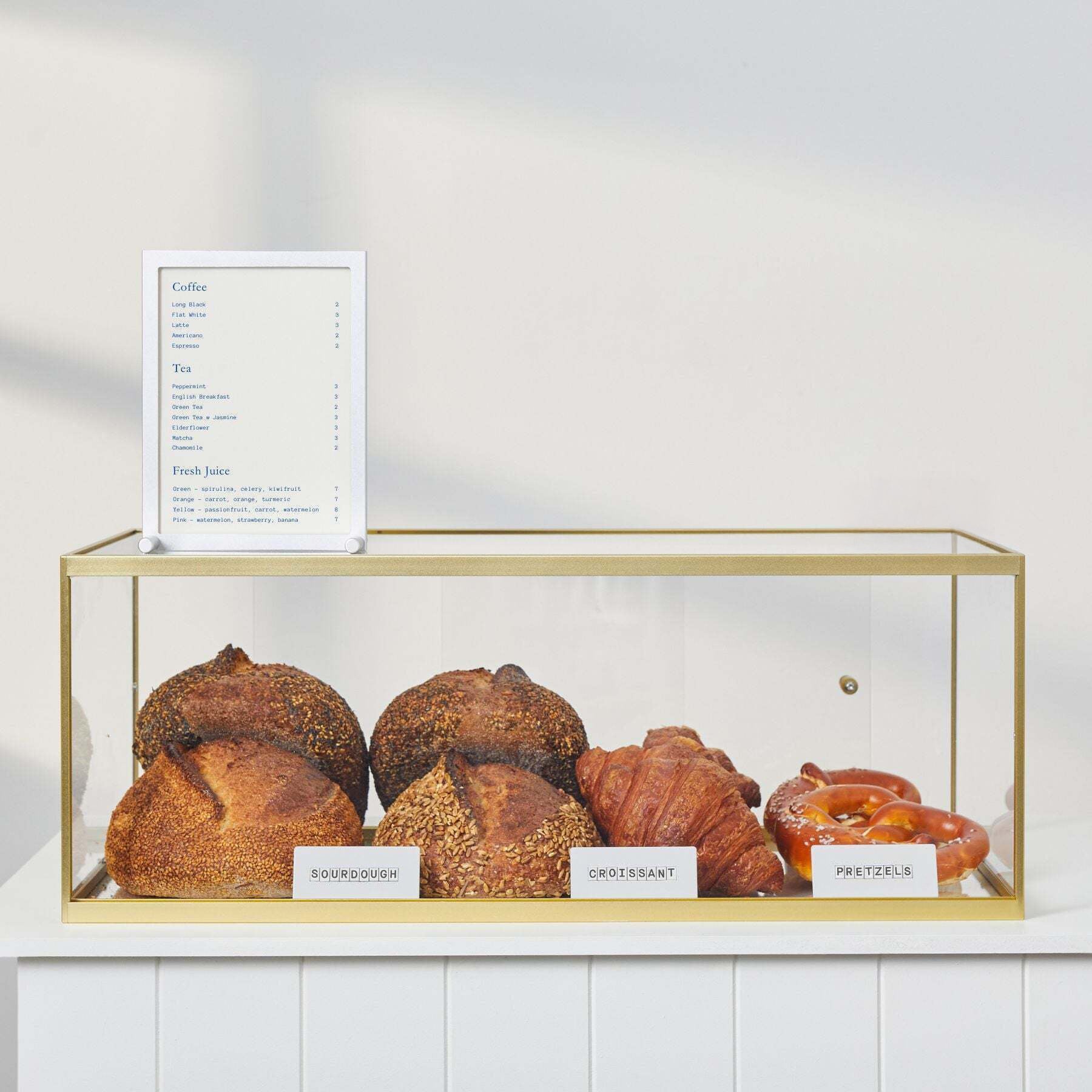 Bakery display case on white counter with assorted breads inside and small menu sign on top