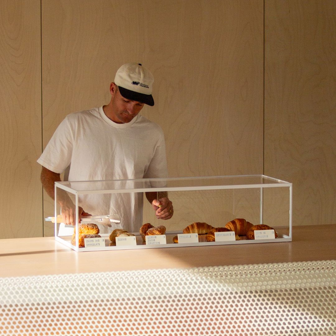 Modern bakery display case filled with small white signs and pastries, and a man arranging pastries