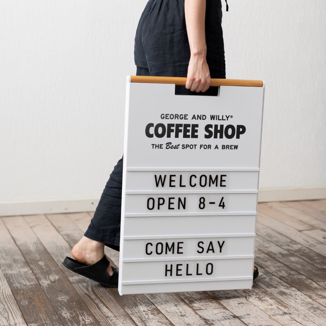 closer up image of person carrying their letter sidewalk pavement sign by its wooden handle