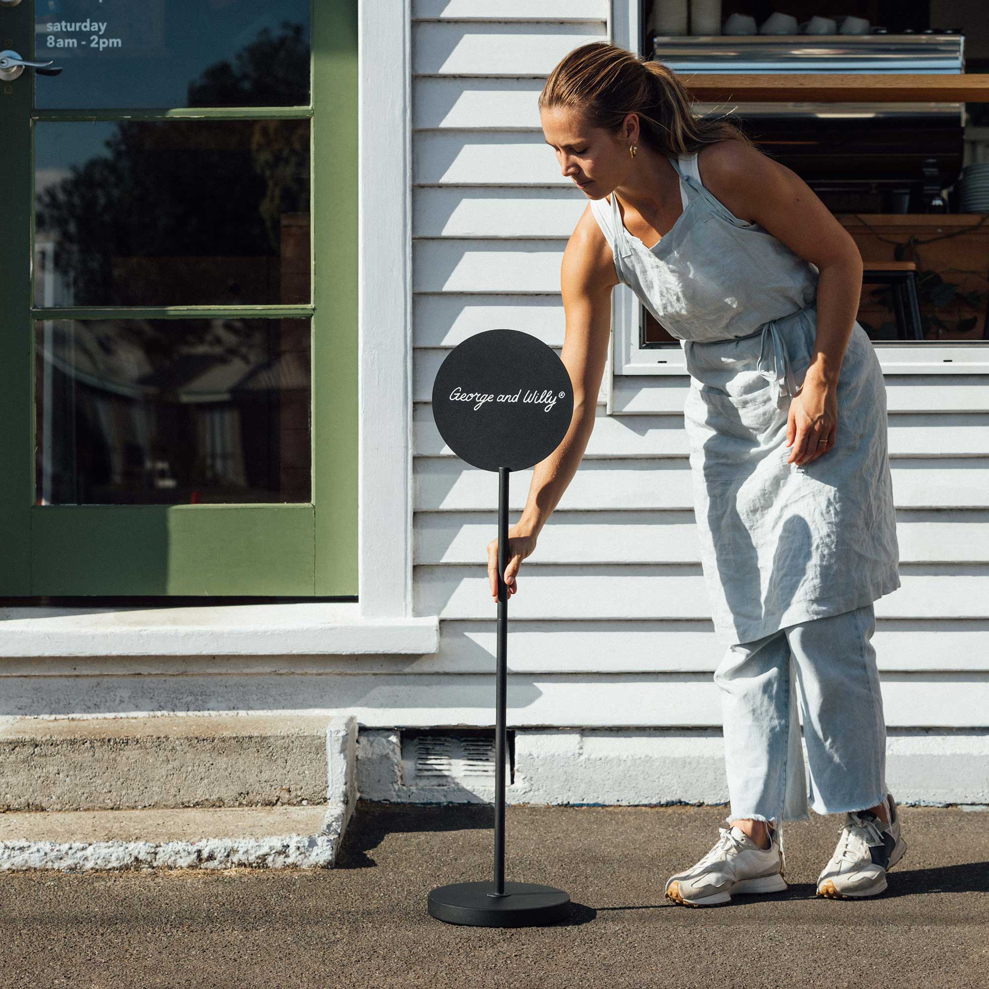 black standing round sign with logo being placed on sidewalk by person