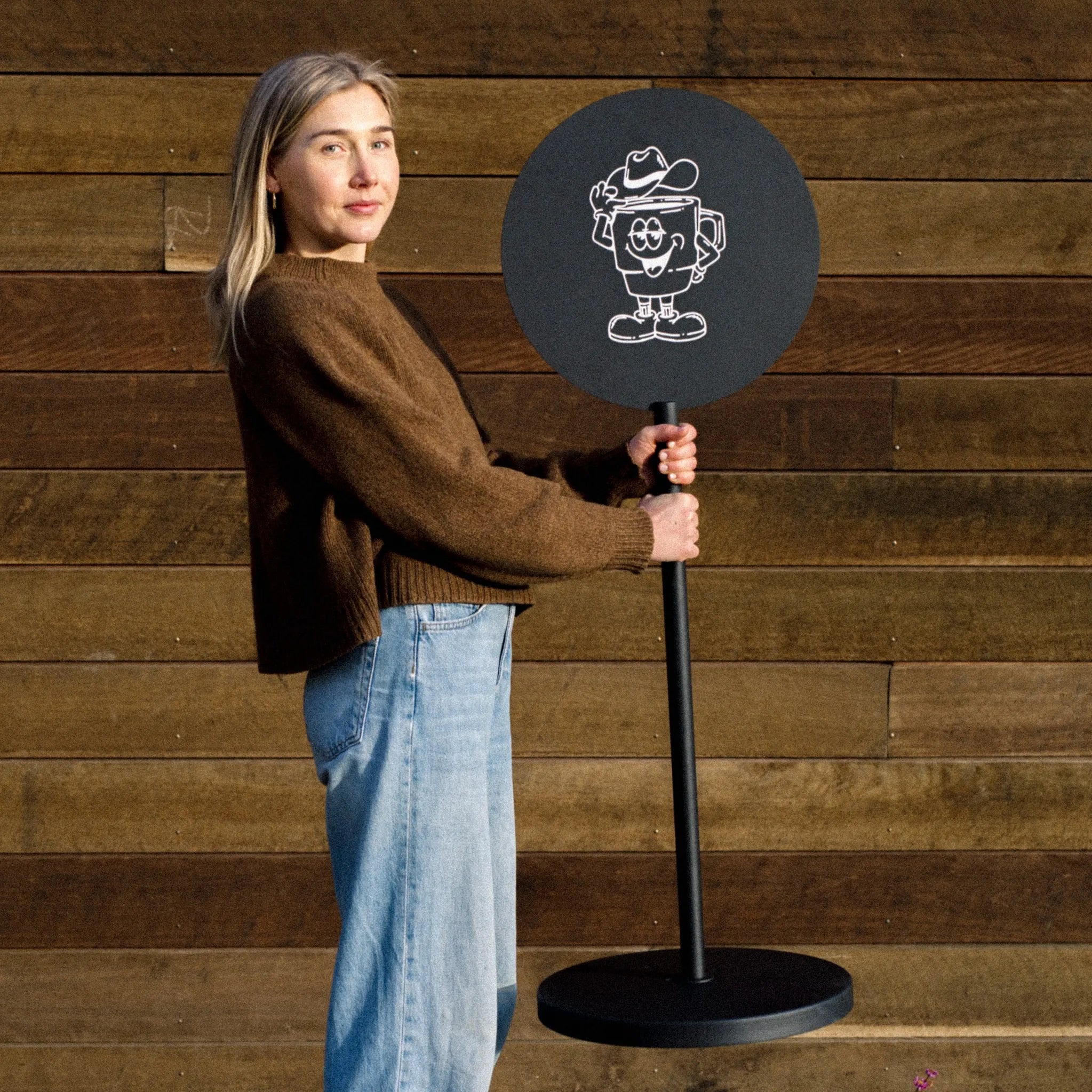 girl lifting and holding the black standing round sidewalk sign and smiling at the camera