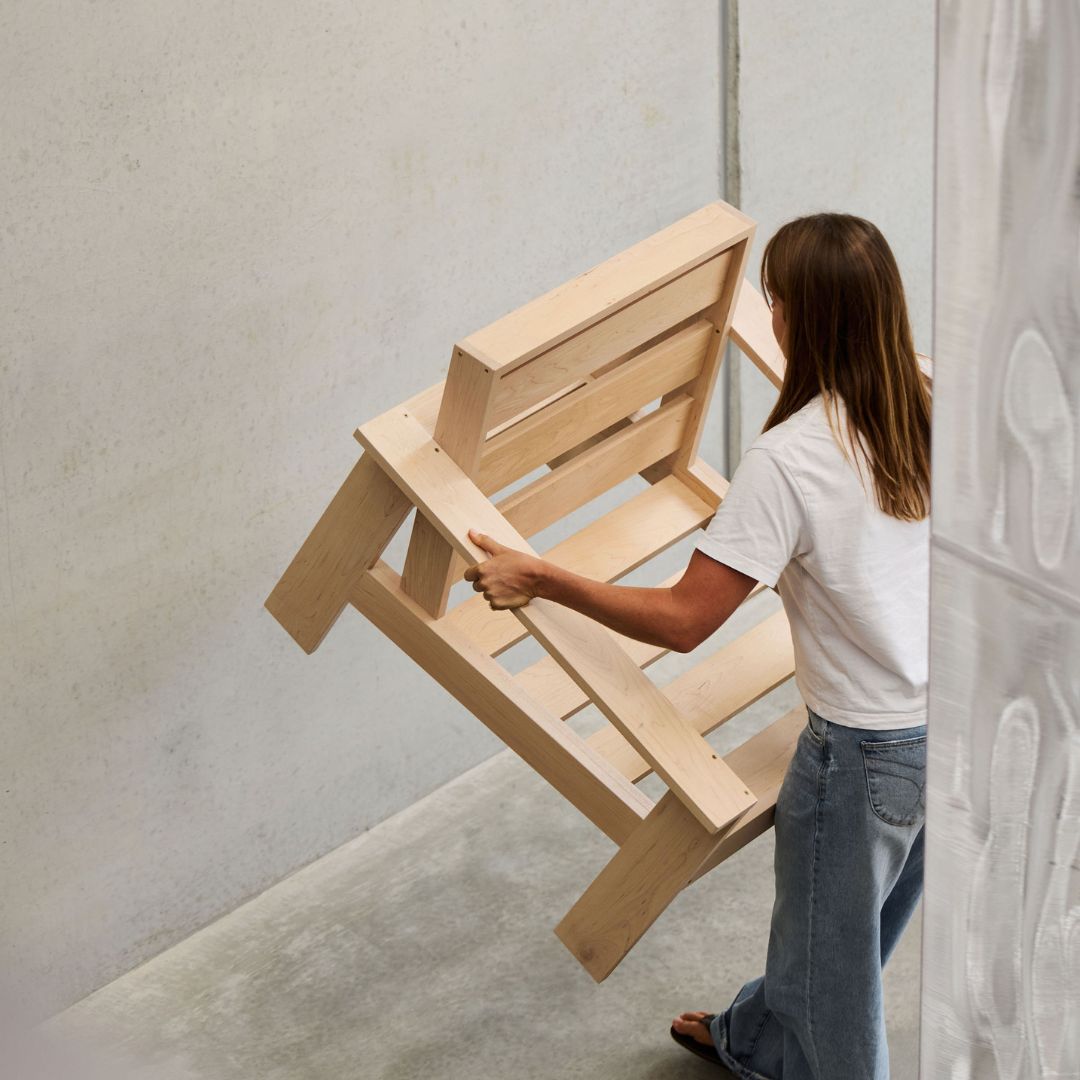 Person lifting  a wooden chair against a light gray wall.